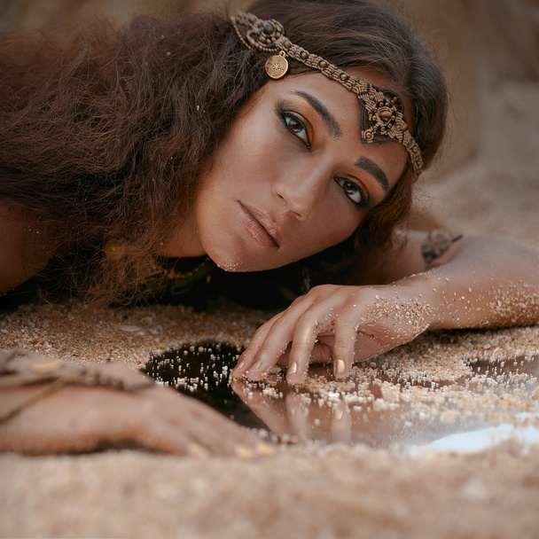 Beautiful girl in ethnic jewelry and mirror covered with sand - Фото, изображение