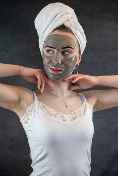 Menina bonita em toalha branca com máscara facial lama verde isolado em preto. Procedimento cosmético, rejuvenescimento e cuidados com a pele. Estilo de vida - Foto, Imagem