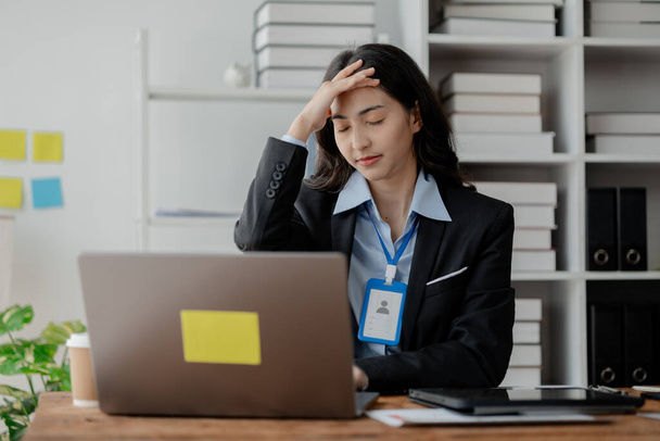 Kobieta siedzi w biurze firmy i wygląda na zestresowaną. Bizneswoman jest zestresowana i zmęczona ciężką pracą. Pracuje od dawna, powodując syndrom biurowy. Koncepcja stresu związanego z pracą. - Zdjęcie, obraz