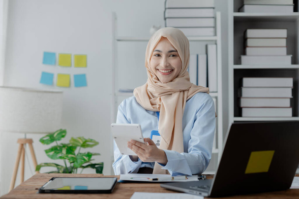 A hidzsábot viselő női munkavállaló az irodában dolgozik, ellenőrzi a vállalat könyvelését és pénzügyeit, hogy biztosítsa a pénzügyek pontosságát és biztonságát. A pénzügyek és számvitel területén végzett munka fogalma. - Fotó, kép