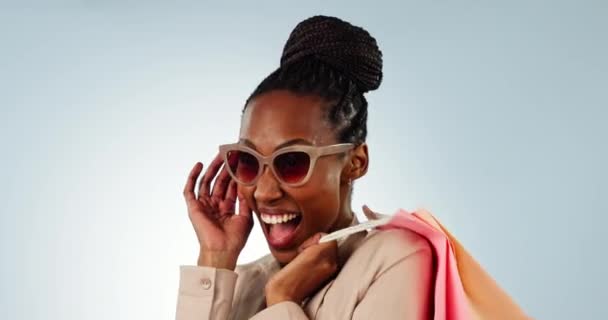 Mujer negra feliz, cara y bolsa de compras con gafas de sol para la moda, el estilo o la compra en un fondo de estudio. Retrato de una mujer africana o sonrisa de comprador para ropa, descuento o venta. - Metraje, vídeo