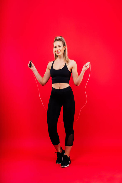 Blond woman with jump rope in a studio, yellow red and dark background - Photo, Image