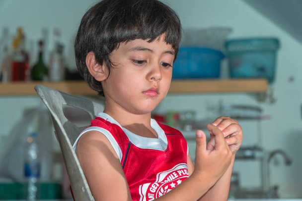 Asiático pequeño niño vistiendo rojo camiseta sentado en la cocina a la espera de una comida - Foto, imagen