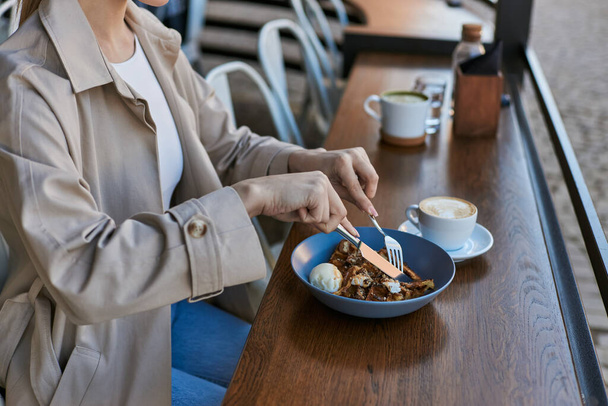 kivágott kilátás nő ballonkabátban eszik belgiai gofri fagylalt mellett egy csésze kávét - Fotó, kép