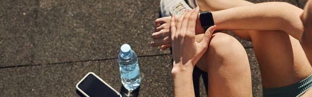banner of sportswoman in activewear checking fitness tracker next to smartphone and water bottle - Photo, Image