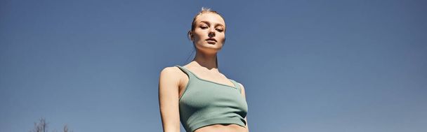 blonde and fit woman in grey crop top standing and looking at camera after workout, banner - Photo, Image