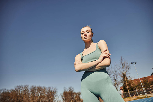 mulher loira e apta em shorts de ciclismo e top corte posando e olhando para a câmera após o treino - Foto, Imagem