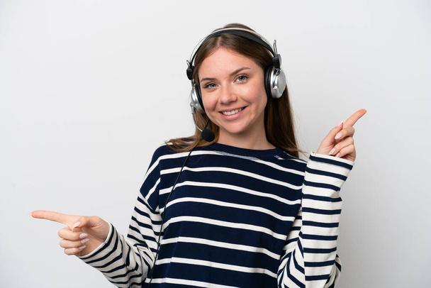 Telemarketer caucasian woman working with a headset isolated on white background pointing finger to the laterals and happy - Foto, imagen