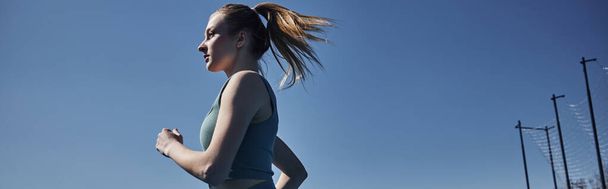 widok z boku blondynka fit kobieta w aktywne odzież działa na zewnątrz, motywacja i sportowy baner - Zdjęcie, obraz