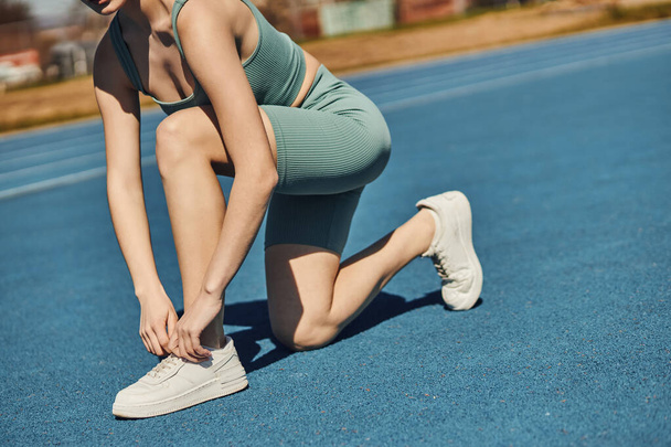 mujer deportiva recortada en ropa deportiva atando cordones en zapatillas blancas antes de correr en pista de jogging - Foto, Imagen