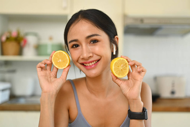 Mujer joven y bonita sosteniendo rodajas de limón y sonriendo a la cámara. Concepto de dieta y estilo de vida saludable. - Foto, Imagen