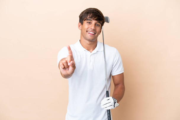 Young golfer player man isolated on ocher background showing and lifting a finger - Foto, Imagen