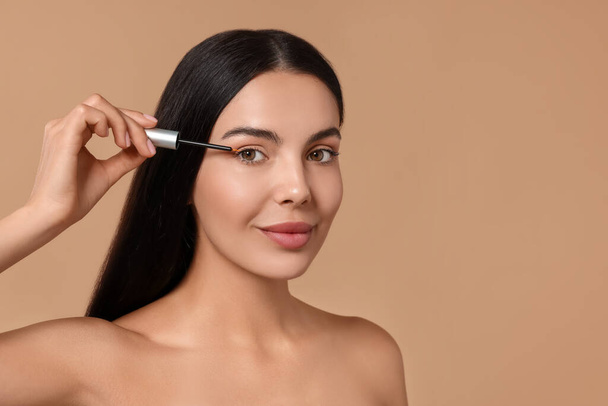 Beautiful woman applying serum onto her eyelashes on beige background, space for text. Cosmetic product - Φωτογραφία, εικόνα