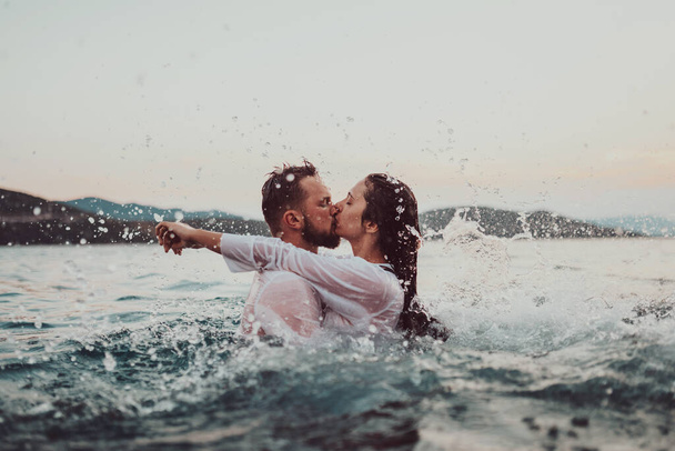 Un jeune couple romantique partageant un baiser passionné au milieu de la beauté sereine de l'océan au coucher du soleil - Photo, image