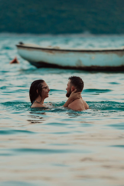 Una romántica pareja joven compartiendo un beso apasionado en medio de la serena belleza del océano al atardecer - Foto, Imagen