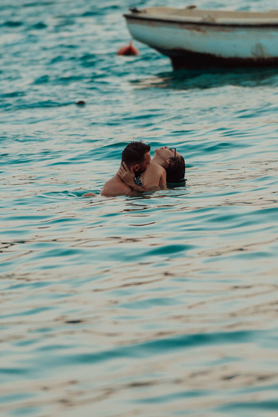 Um jovem casal romântico compartilhando um beijo apaixonado em meio à beleza serena do oceano ao pôr do sol - Foto, Imagem