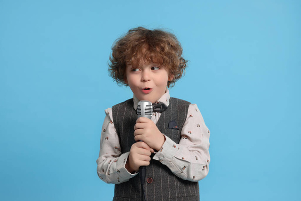 Cute little boy with microphone singing on light blue background - Fotoğraf, Görsel