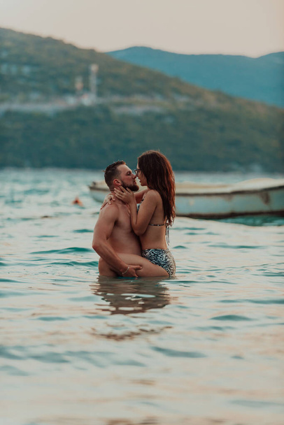 Günbatımında okyanusun dingin güzelliği arasında tutkulu bir öpücüğü paylaşan romantik genç bir çift. - Fotoğraf, Görsel