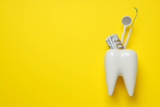 Стоматологічні інструменти та гроші в декоративному зубі на жовтому тлі, простір для тексту - Фото, зображення