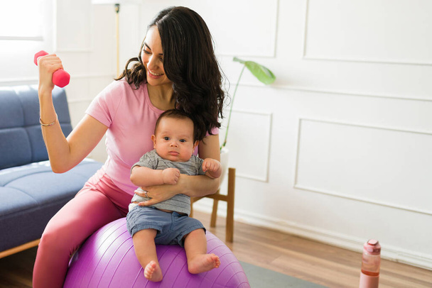 フィットアクティブママ持ち上げダンベルウェイトと自宅で彼女の新生児の世話をしながら安定ボールで運動 - 写真・画像