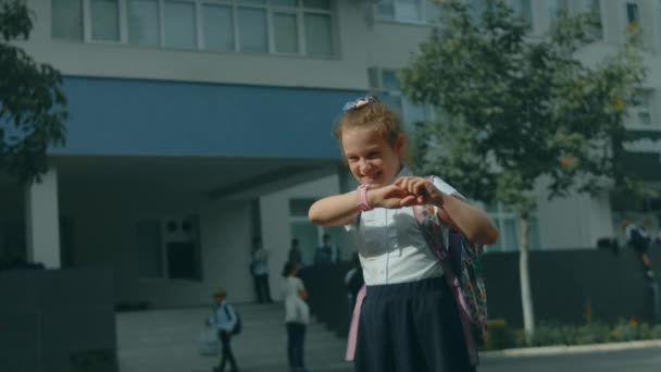 Kaunis valkoihoinen koulutyttö käyttää älykelloa ulkona koulupuistossa luokkien jälkeen. Onnellinen lapsi puhuu vanhempiensa kanssa videopuhelussa älypuhelimella. Smart rannekello GPS tracker - Materiaali, video