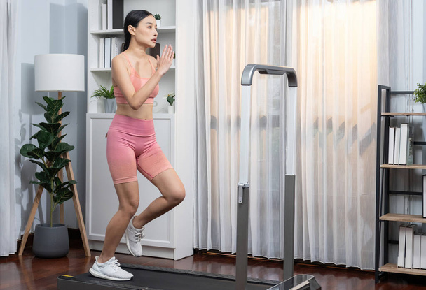 Energetikus és erős sportos ázsiai nő fut futógéppel otthon. Üldözése fit fizikum és elkötelezettség az egészséges életmód otthoni edzés és képzés. Élénk. - Fotó, kép