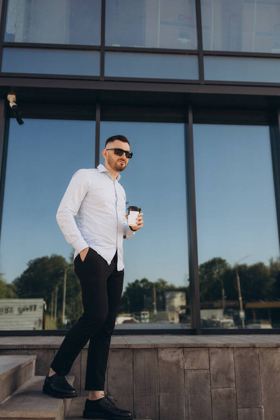 Впевнений молодий бізнесмен використовує мобільний телефон і п'є каву в місті. Високоякісна фотографія - Фото, зображення