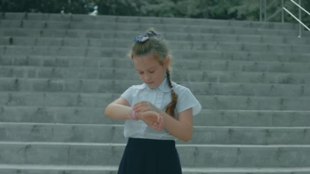 Lächelndes süßes Schulmädchen, das mit der Smartwatch spielt. Fröhliche 8-Jährige Mädchen spricht auf Smartwatch. Kind im Park im Freien - Filmmaterial, Video