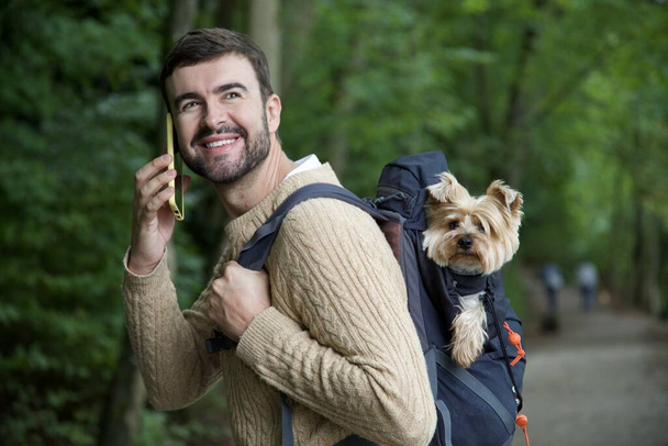 ritratto di bel giovane felice che viaggia con il suo cane carino nello zaino - Foto, immagini
