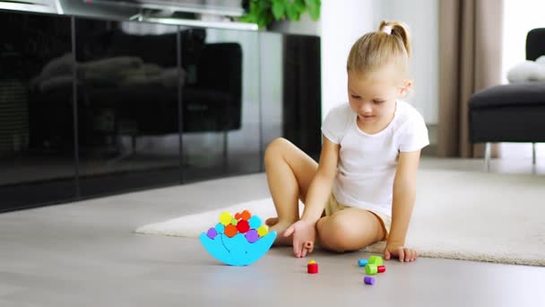 Bambina che gioca con il giocattolo di bilanciamento in legno sul pavimento nel salotto di casa. Filmati 4k di alta qualità - Filmati, video