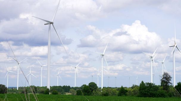 Postępowy sposób wykorzystania wiatru jako odnawialnego źródła energii do zasilania nowoczesnego stylu życia przez farmę turbin wiatrowych na zielonym polu lub wzgórzu. Generator wiatraków wytwarza energię elektryczną bez emisji CO2. - Zdjęcie, obraz