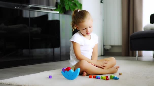 Bambina che gioca con il giocattolo di bilanciamento in legno sul pavimento nel salotto di casa. Filmati 4k di alta qualità - Filmati, video