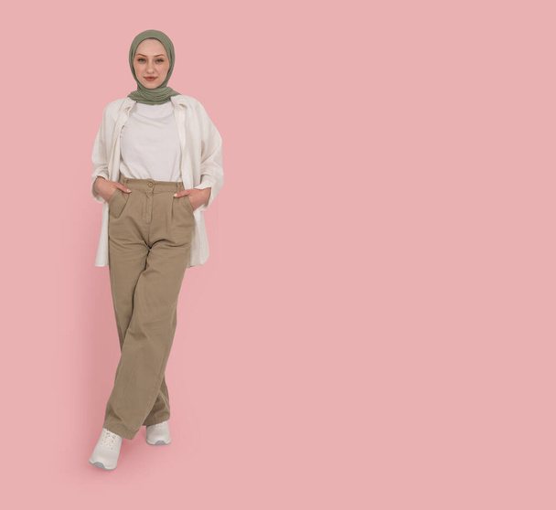 Vue complète du corps jolie fille musulmane porter abaya hijab mettre les mains poches souriant caméra regardant debout sur le portrait studio rose clair. Peuple islam concept religieux image, copier l'espace. - Photo, image