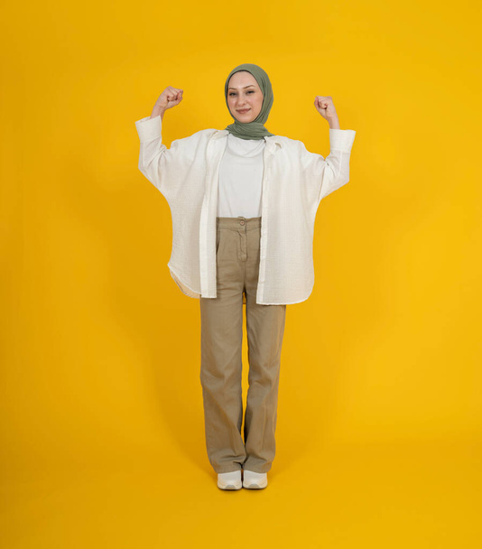 Повна довжина тіла вид спереду молода усміхнена горда впевнена щаслива молода жінка в хіджаб-абаї робить жест переможця, відзначаючи клейкі кулаки. Ізольований жовтий студійний фон. концепція ісламського способу життя - Фото, зображення