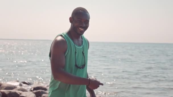 Średnie spowolnienie szczęśliwego młodego czarnego mężczyzny rzucającego frisbee podczas zabawy z dzieckiem na piaszczystej plaży w słoneczny dzień - Materiał filmowy, wideo