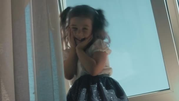 Schöne lockige Mädchen sitzt auf der Fensterbank lächelnd und genießt ihre Zeit zu Hause - Filmmaterial, Video