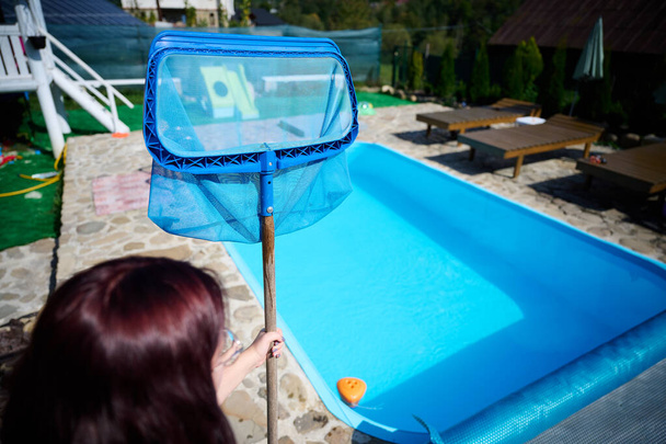 Nuori nainen puhdistaa uima-altaan. Henkilökunta siivoaa uima-allasta aurinkoisena kesäpäivänä. Hotellin työntekijä siivoamassa allasta. Siivoan uima-allaspalvelua. Puhdistus verkolla. - Valokuva, kuva