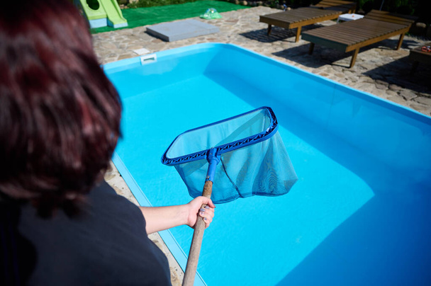 Nuori nainen puhdistaa uima-altaan. Henkilökunta siivoaa uima-allasta aurinkoisena kesäpäivänä. Hotellin työntekijä siivoamassa allasta. Siivoan uima-allaspalvelua. Puhdistus verkolla. - Valokuva, kuva