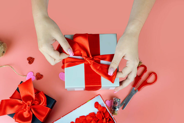 Valentinstag-Konzept. Großaufnahme weiblicher Hände, die Geschenke mit roter Schleife verpacken. handgefertigte Tischdekoration - Foto, Bild