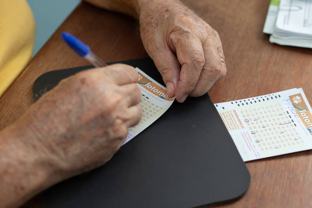Close-up on the hands of an elderly man who is marking the numbers on a lottery game card. - Foto, Imagen