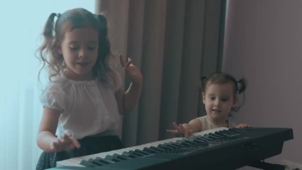 Kaukázusi fiatal zenész lány gyerek szórakozás tevékenységek zongorázni zenei leckét zeneoktatás otthon. Toddler húga is játszani próbál. Érezzétek jól magatokat. - Felvétel, videó