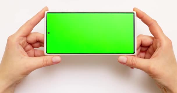 Женские руки держат смартфон с зеленым экраном на белом фоне. Высококачественные 4k кадры - Кадры, видео
