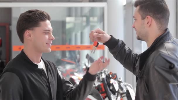 Motorbike dealer putting motorcycle keys in buyers hand. Ligtly bearded consultant made deal with client. Young caucasian man smiling after he got the motorcycle keys - Footage, Video