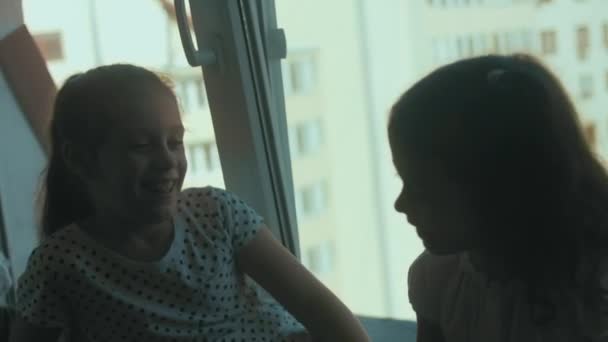 Zwei Schwestern haben Spaß, reden und erzählen Geschichten, sitzen auf der Fensterbank neben dem großen Fenster.. - Filmmaterial, Video