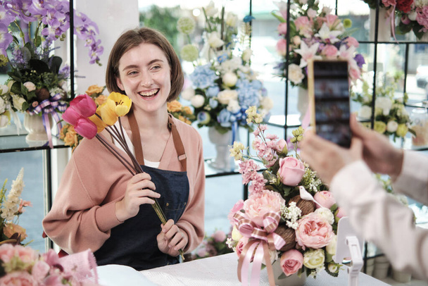 Електронна комерція бізнес, одна молода біла жінка-флорист демонструє і показує квіткові композиції через онлайн трансляції з додатком смартфона в магазині яскравих квітів, красивий магазин квітів
.  - Фото, зображення