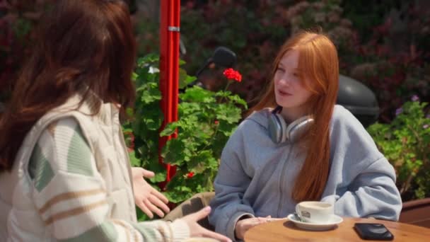 Twee tienermeisjes met pauze in cafe drinken koffie buiten zonnig weer zomer lente. Jonge vrouwen praten, roddelen, kletsen, plezier hebben.  - Video