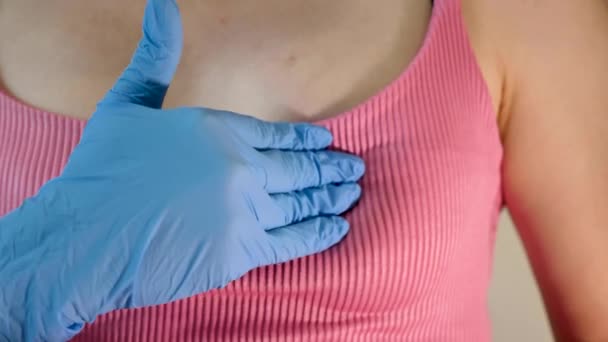 Een mammoloog in een medische handschoen controleert de borsten van een jonge vrouw op borstkanker in een kliniek voor Internationale Kankerdag. Close-up - Video