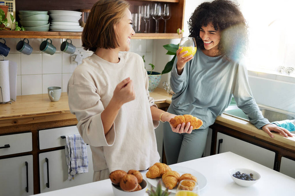 Paar, Glück und Frauen mit Saft und Kochen in der Küche zum Frühstück, Ernährung und Vitamin C am Morgen. Essen, Leute und Lächeln mit Getränken und Schlafanzug oder natürlichem Gesicht für Wellness oder Obst. - Foto, Bild