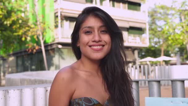 Pozitív fiatal nő alkalmi ruhákban mosolyog és belenéz a kamerába városképben.4k - Felvétel, videó
