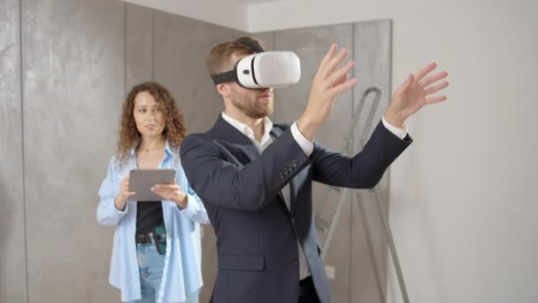 Giovane uomo in giacca e cravatta e donna designer in piedi in camera nel nuovo appartamento durante la ristrutturazione indossando occhiali VR utilizzando tecnologie futuristiche per progettare casa, realtà virtuale, concetto di ristrutturazione - Filmati, video